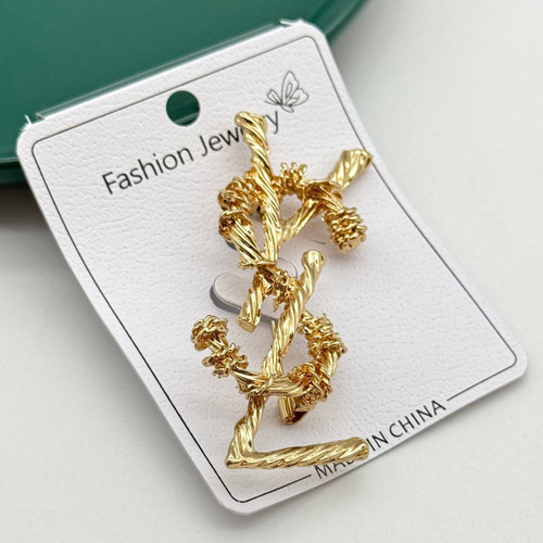 گل سینه طلایی زنانه با طرح لوگوی حروف درهمتنیده و بافت پیچدار