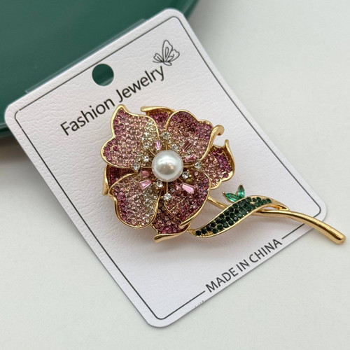 گل سینه طلایی طرح گل با نگینهای صورتی، ساقه سبز و مروارید سفید در مرکز