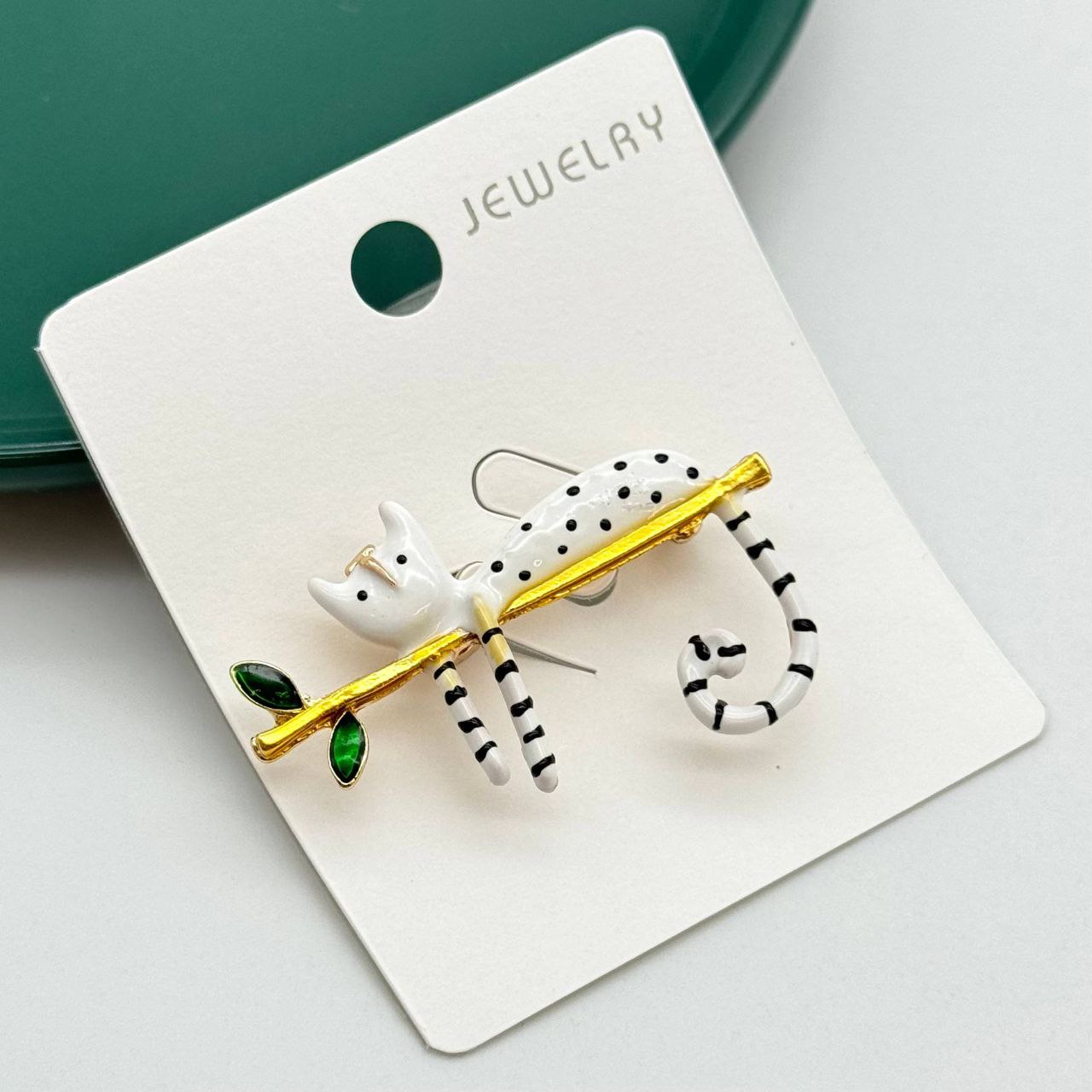 گلسینه فانتزی مدل گربه سفید خالدار در حال استراحت روی شاخه درخت طلایی با برگهای سبز.