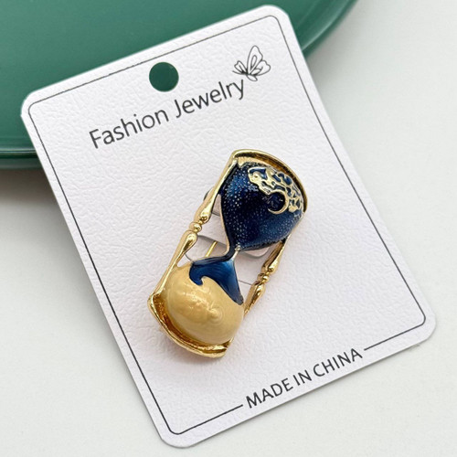 گل سینه فانتزی طلایی با طرح ساعت شنی، میناکاری شده به رنگ سرمهای اکلیلی و کرم.