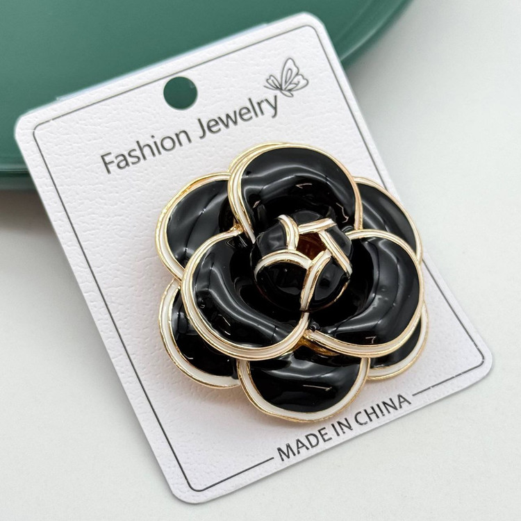 گل سینه مشکی براق طرح گل کاملیا با حاشیه سفید و طلایی.