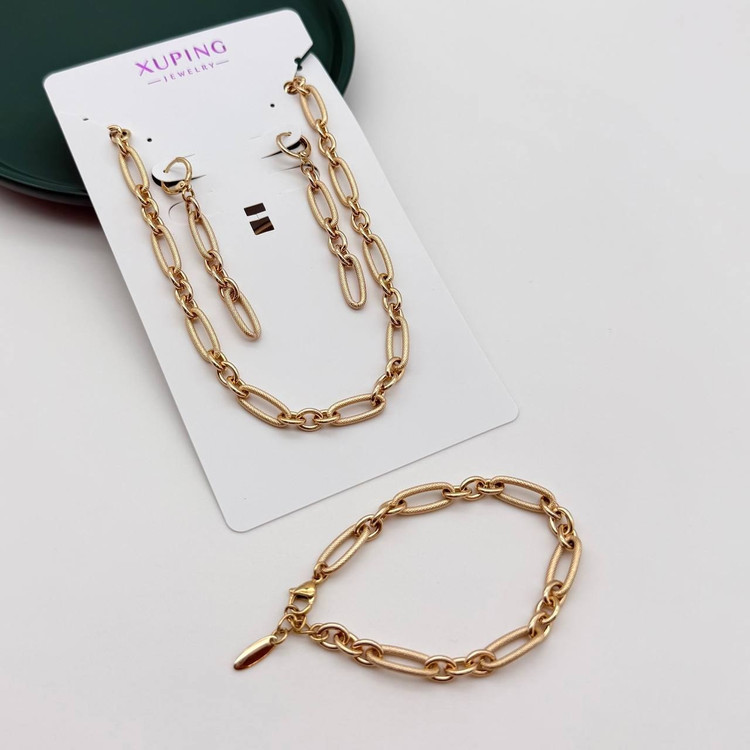 تصویر استودیویی از سرویس کامل زیورآلات ژوپینگ (XUPING) رنگ طلایی مدل زنجیر لینک (Cartier/Paperclip) با بافت تراشدار روی حلقهها، شامل گردنبند و گوشواره روی کارت مقوایی برند و دستبند ست جداگانه.
